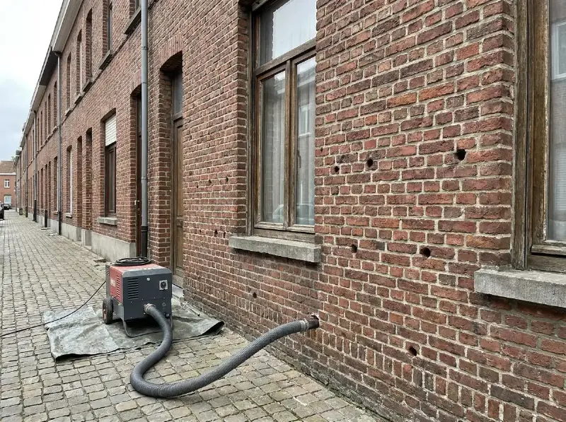 Boorgaten in de voegen van een bakstenen gevel waarlangs isolatieparels in de spouw worden geblazen