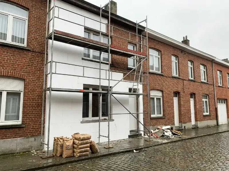 Steiger voor een rijwoning met isolatieplaten half aangebracht op de gevel en zakken lijmmortel op de stoep
